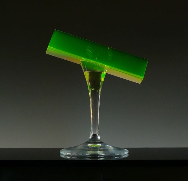 Titel: Atomic Green Design, utförande och foto: Anna Carlgren Material: Prismat är slipat och polerat av massivt uranhaltigt glas som limmats på en hyttarbetad fot av helkristall (33% blymönja, Pb3O4) Höjd: 15 cm Anna Carlgren slipar med kiselkarbid (SiC) på gjutjärnsskivor, finslipar med aluminiumoxid ( Al2O3) och polerar på tagel med ceriumoxid (CeO2)